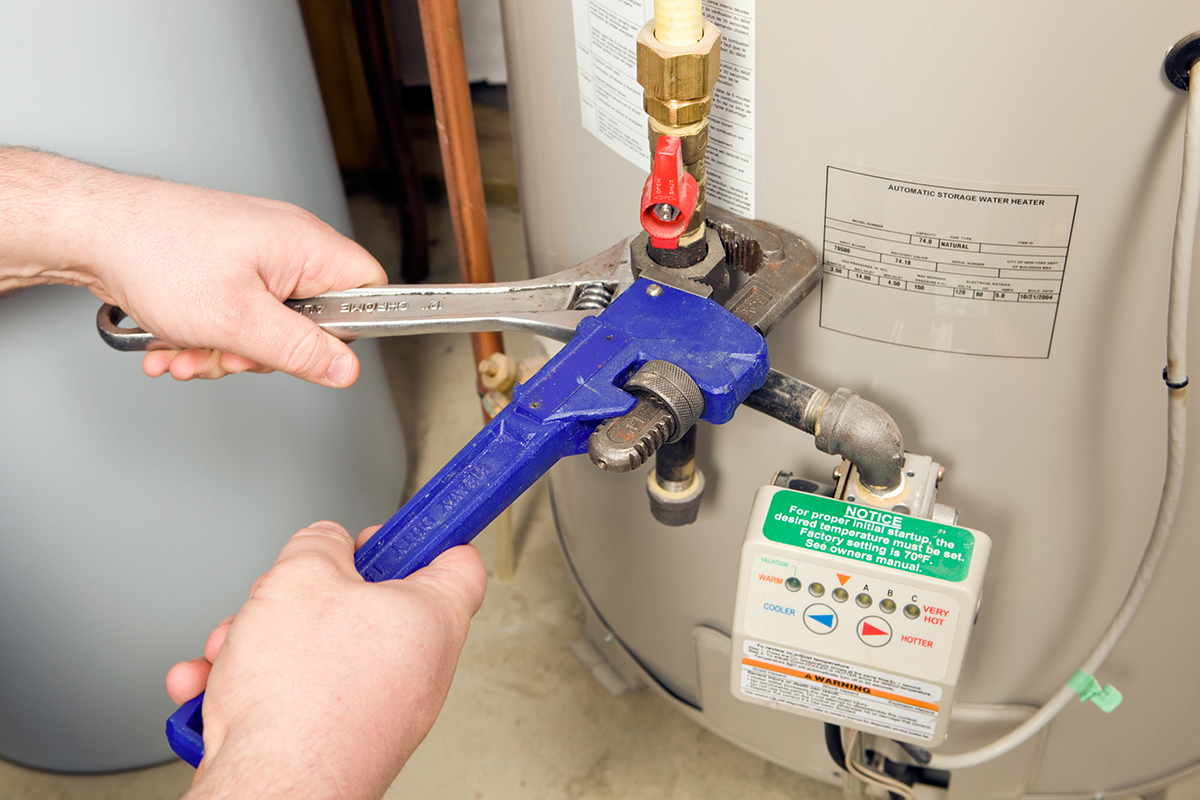 A person uses a pipe wrench to tighten a valve on a water heater.